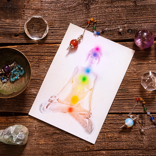 Chakras illustrated over human body with natural crystals and pendulum